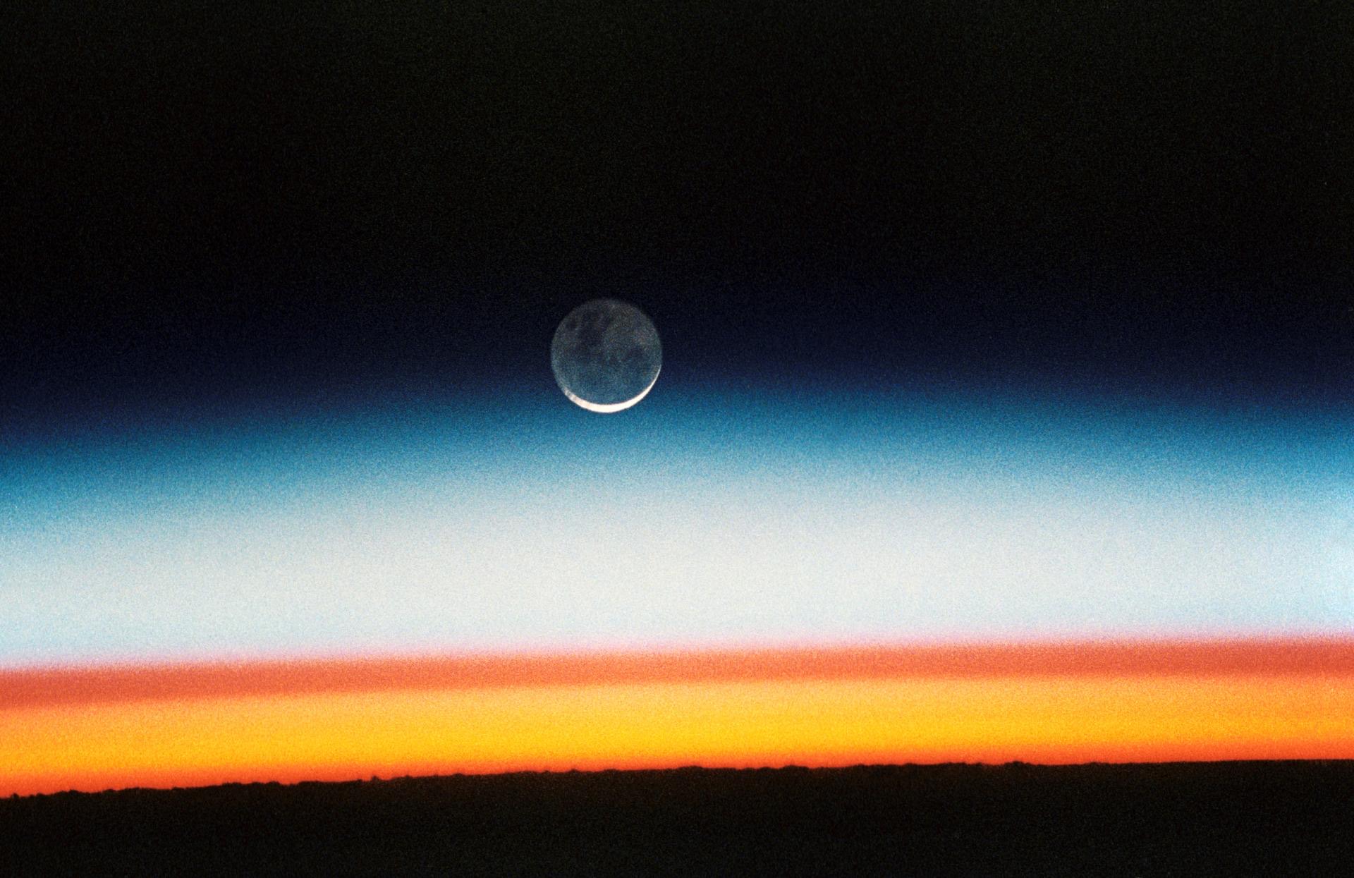 Sunrise across the curve of Earth, a thin blue band of atmosphere against black space.