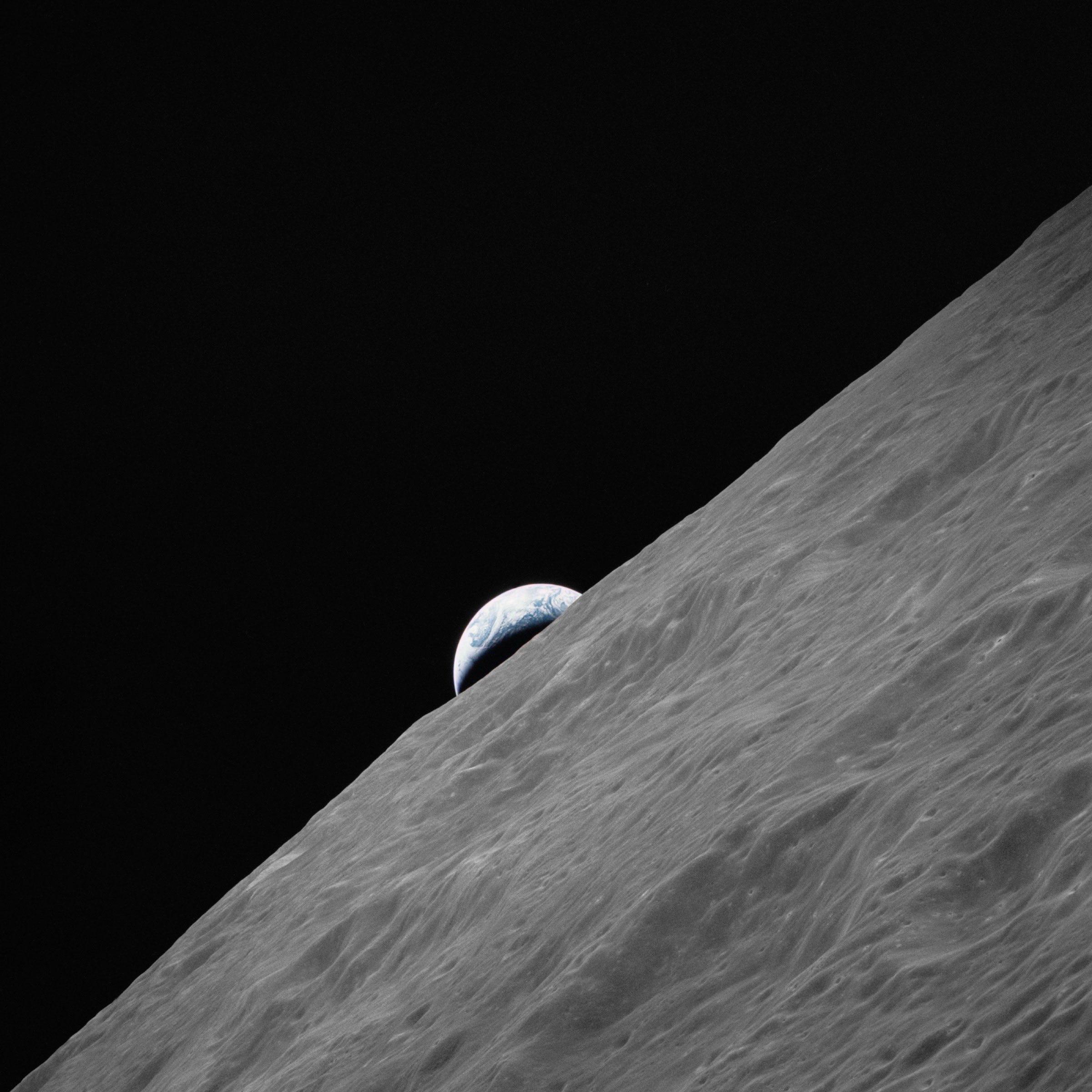 Earth as a small crescent rising above the curve of the Moon, against black space.