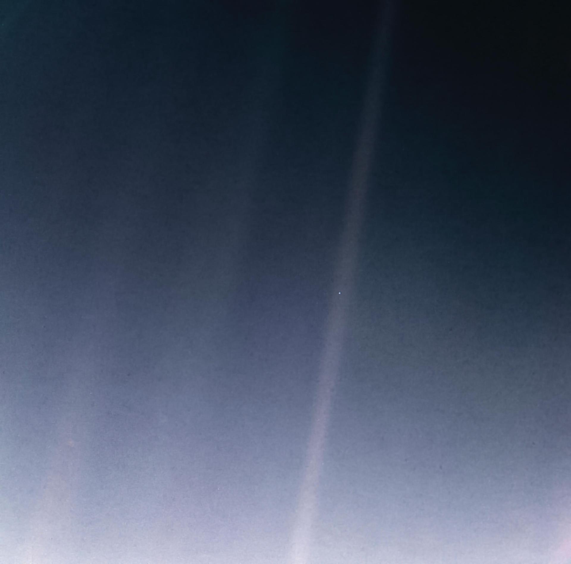 Earth as a single pale point of light in a band of scattered sunlight.
